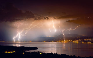 Different lightning bolts striking over the smooth water surface