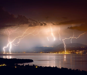 Different lightning bolts striking over the smooth water surface